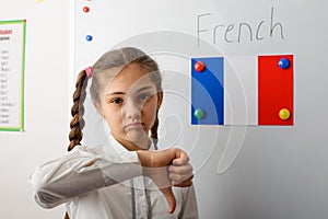 Schoolgirl showing thumbs down at the clcassroom with a French flag on the board