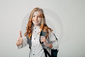 Schoolgirl shows thumb up and goes to study lessons. A cheerful student with red hair is happy to go to acquire new