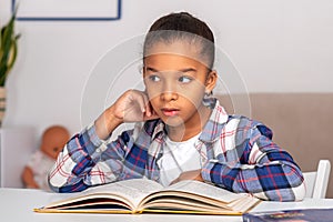 The schoolgirl siting at the table indoors and doing his homework