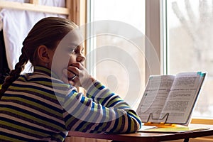 A schoolgirl sits at a table by the window and does her homework, the girl was distracted in thought and looked towards the frame