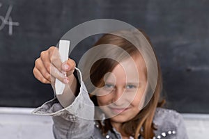 The schoolgirl, sitting at the bench, extends her hand with chalk up and reports to answer