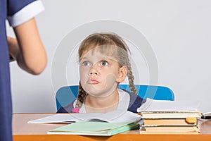 Schoolgirl sitting at the desk angrily looks at another girl photo