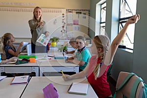 Schoolgirl sitting at a desk raising her hand in an elementary school classroom