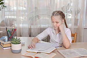 Schoolgirl sitting at desk and reading book. Education Back to school