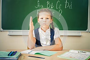 Schoolgirl sitting at desk, school classroom, on background of board