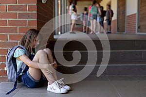 Schoolgirl  sitting on the ground alone in the schoolyard at elementary school