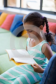 Schoolgirl sitting on sofa and reading book in library