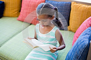 Schoolgirl sitting on sofa and reading book in library