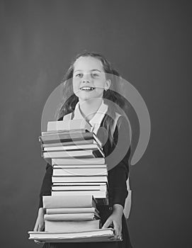 Schoolgirl with smiling face holds huge pile of books