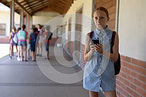 schoolgirl standing in the schoolyard at elementary school using a smartphone