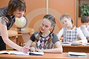 Schoolgirl is studying. School kids work at lesson. Teacher controlling learning process.