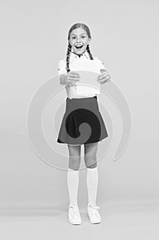 Schoolgirl studying textbook. Exciting literature. Girl child hold book stand yellow background. Kid girl school uniform