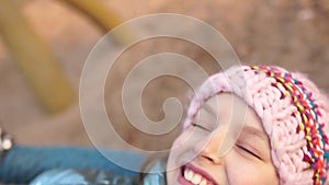 Schoolgirl swinging on a swing on the playground during the winter holidays. The girl wears a pink knitted hat. Close up