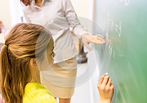 Schoolgirl and teacher writing on chalk board