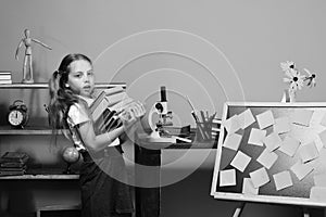 Schoolgirl with tired face. Girl carries pile of books to desk with microscope