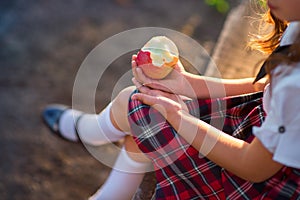 Schoolgirl in uniform is eating an apple in the park.