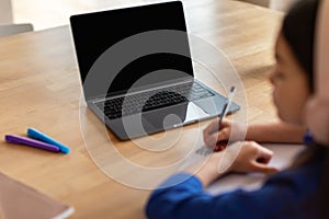 Schoolgirl using laptop with empty screen taking notes indoor