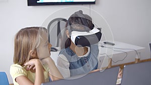 Schoolgirl in VR headset sitting at desk near classmate