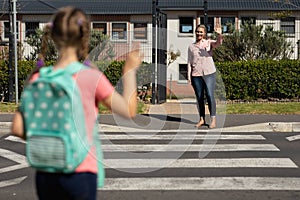 Schoolgirl waving to her mother at a pedestrian crossing