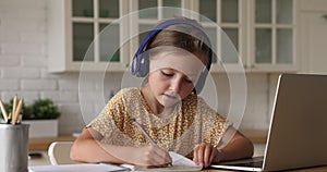 Schoolgirl wear headphones listen audio on laptop writes in copybook