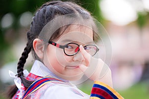 Schoolgirl wearing young girl's uniform. Child uses the index finger to push the glasses she is wearing. Sweet smile.