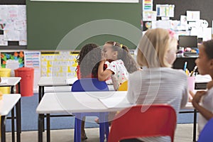 Schoolgirl whispering into her friend ear in classroom at school