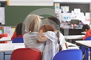 Schoolgirl whispering into her friend ear in classroom at school