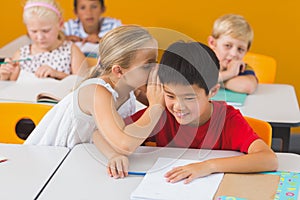 Schoolgirl whispering into her friend s ear in classroom