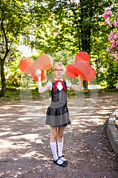 A schoolgirl in a white blouse with a red tie, with a bow and red balloons in the class. Back to school concept