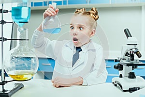 Schoolgirl in white coat making experiment with reagents in chemical lab