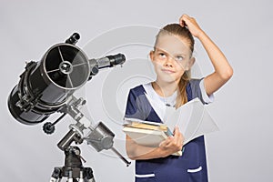 Schoolgirl wondered and looked up to by reading a textbook while standing at the telescope