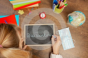 Schoolgirl writes in chalk on a small blackboard `Quarantine`.