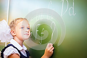 Schoolgirl writes English alphabet with chalk on blackboard