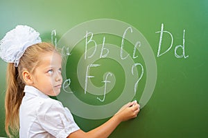 Schoolgirl writes English alphabet with chalk on blackboard