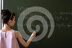 schoolgirl writing high school maths formula with chalk on blackboard