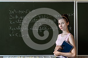 schoolgirl writing high school maths formula with chalk on blackboard