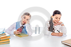 Schoolgirls in formal wear sitting at desk with books and writing Isolated On White.