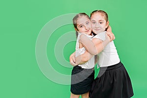 Schoolgirls hug each other on green background. School friendship. Best friends