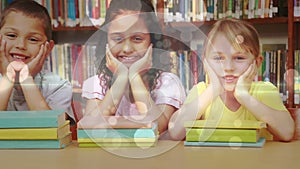 Schoolgirls leaning on a table and looking at the camera with books in front of them in a library