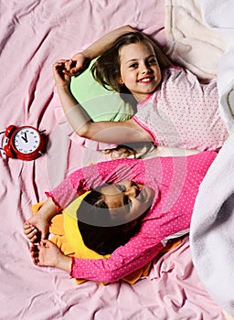 Schoolgirls in pink pajamas wallow on colorful pillows, top view