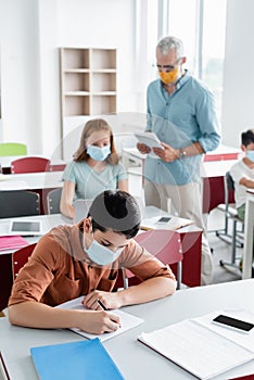 Schoolkid in medical mask writing on