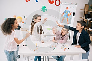 Schoolkids giving high five while studying with molecular model in classroom