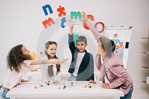 Schoolkids giving high five while studying with molecular model in classroom