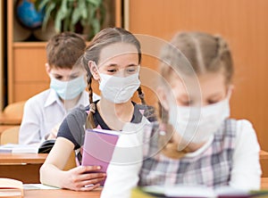 Schoolkids with medicine mask on faces against virus in classroom