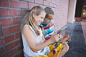 Schoolkids sitting in corridor and using digital tablets