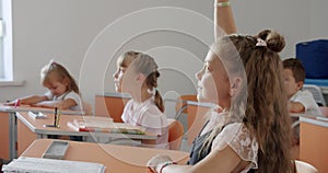 schoolkids sitting at desks in classroom and then raising their hands to answer.