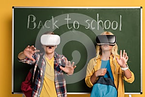 Schoolkids with Virtual reality headsets standing near chalkboard with back to school lettering