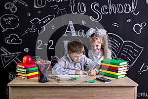 Schoolkids working at the desk with books, school supplies. Left-handed boy writing the text and smiling girl looking at