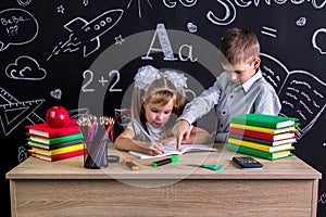 Schoolkids working at the desk with books, school supplies. Right-handed girl writing the text on the exercise book and