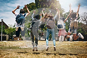 Schools out. Rearview shot of a group of unidentifiable schoolchildren jumping in the park.